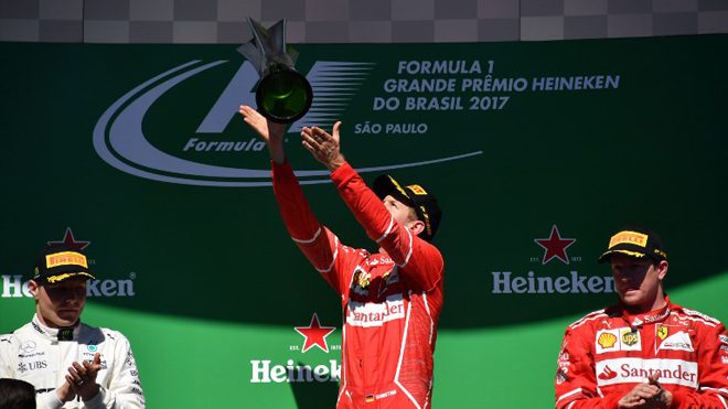 Ferrari's German driver Sebastian Vettel (C) celebrates on the podium with his trophy after winning the Brazilian Formula One Grand Prix as runner-up Mercedes' Finnish driver Valtteri Bottas and third-place Ferrari's Finnish driver Kimi Raikkonen applaud, at the Interlagos circuit in Sao Paulo, Brazil, on November 12, 2017. Nelson ALMEIDA / AFP
